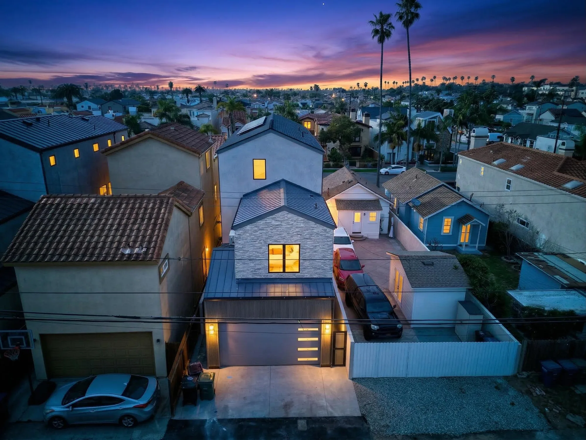 Twilight aerial drone photo of modern three-story beach home with pink sunset sky