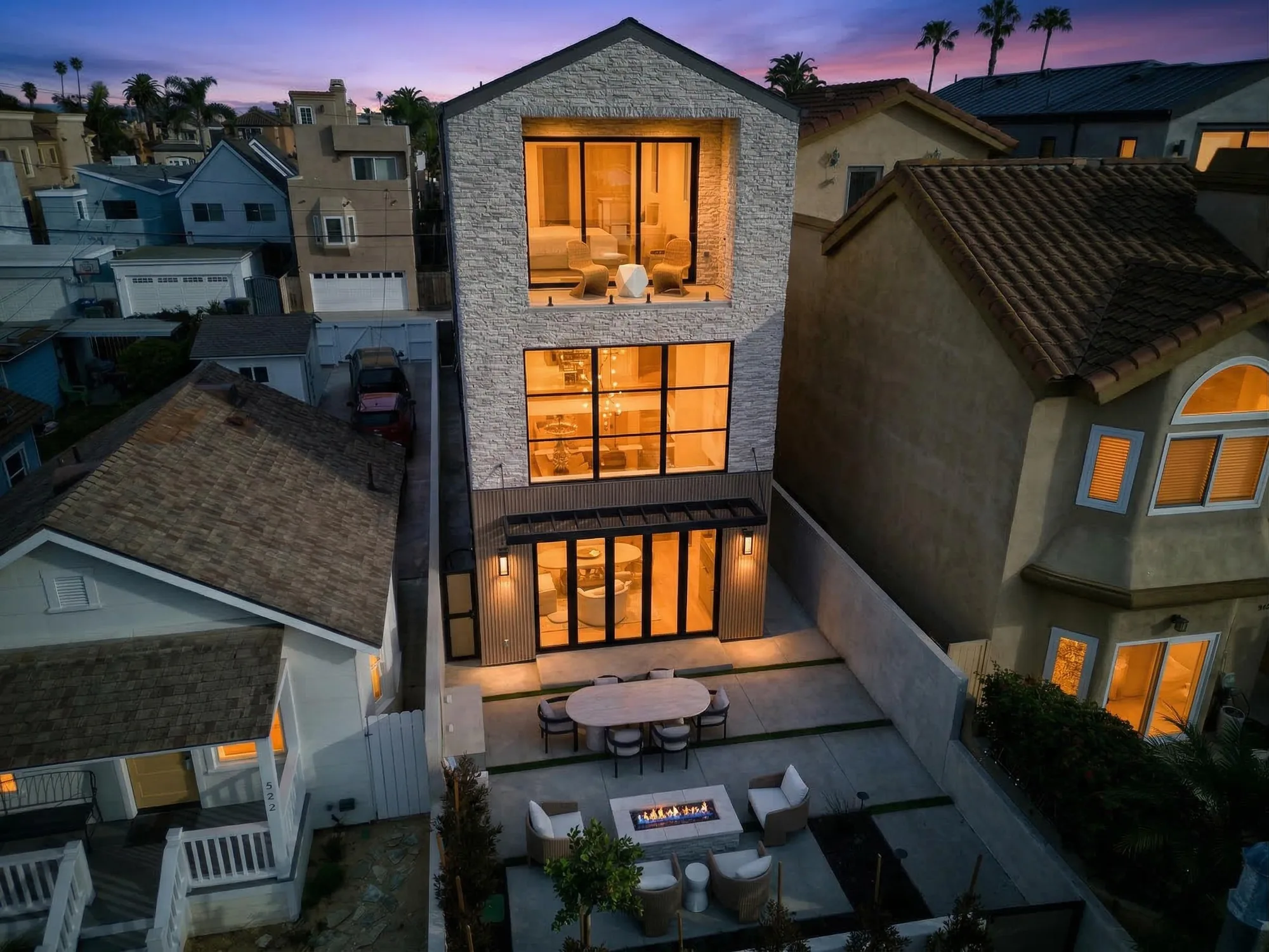Twilight aerial drone photo of modern three-story luxury home with stone facade