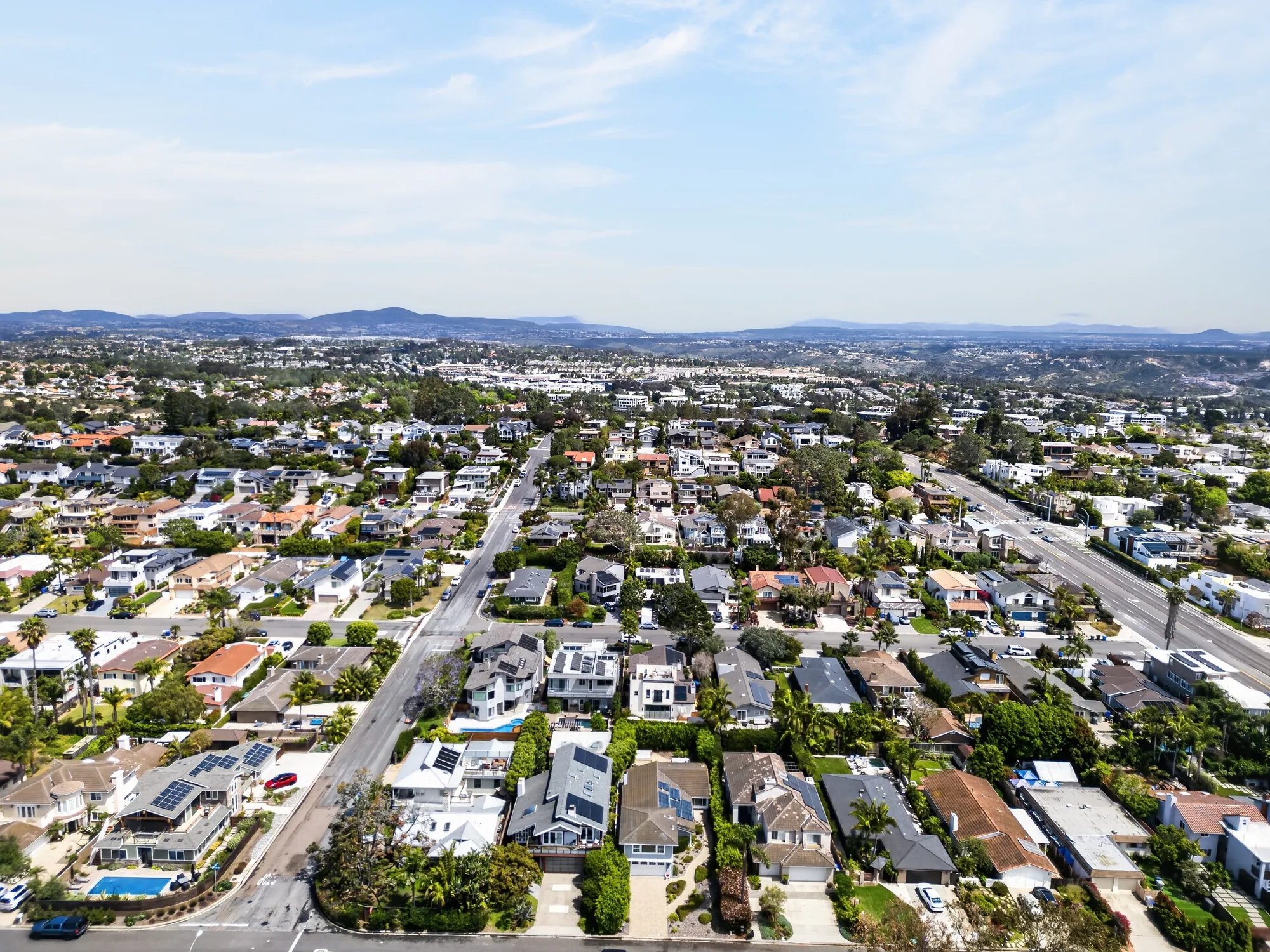 Wide aerial drone photo of coastal neighborhood facing inland toward distant mountains