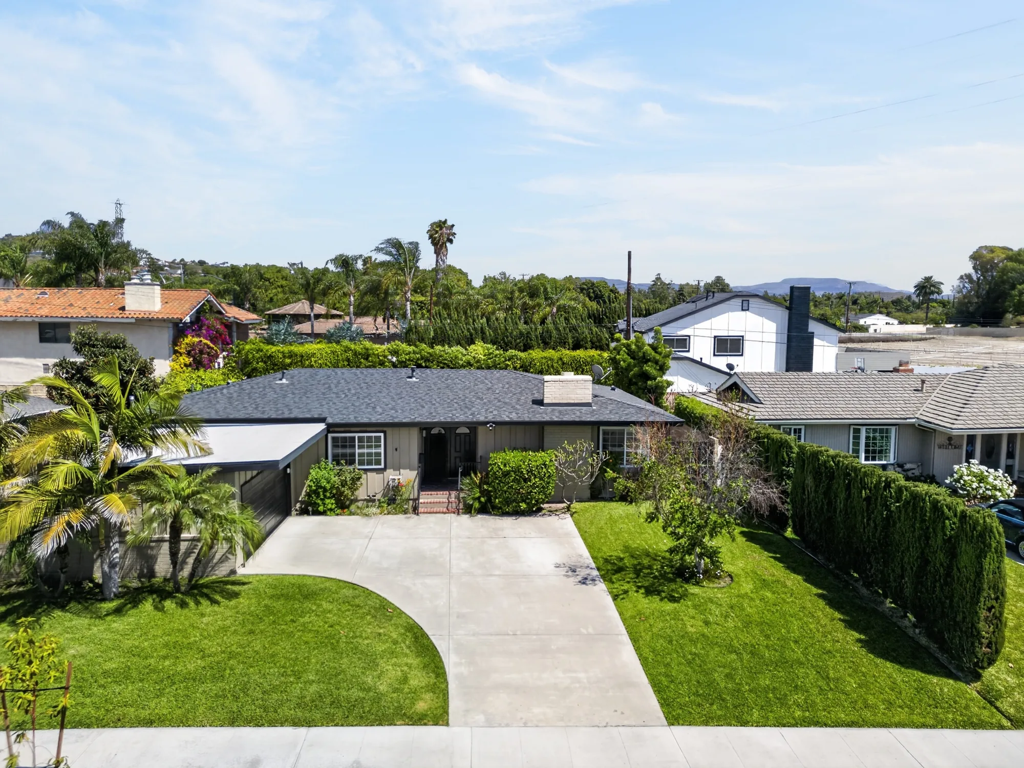 Daytime drone photo of ranch-style single-story home with palm trees